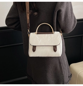 Model view of cream textured handbag with gold metal handle and wide fabric strap