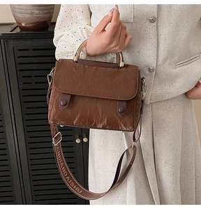 Detail of a brown textured crossbody bag with golden curved handle and wide shoulder strap