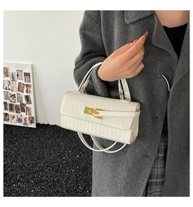 Detail der cremeweißen Handtasche mit Webstruktur und goldenem Schloss am grauen Mantel