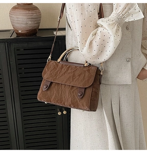 Detail of dark brown wrinkled leather bag with golden arched handle and woven strap