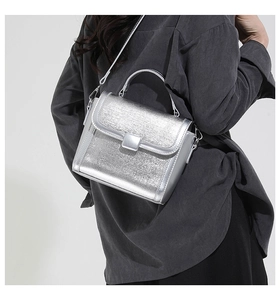 Detail of silver metallic textured square bag with polished finish and metal hardware