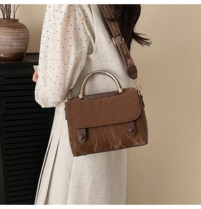 Detail of brown pleated handbag with golden circular handle and branded wide textile strap