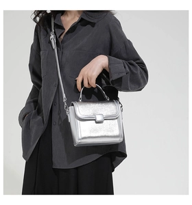 Detail of silver metallic textured crossbody bag with square buckle and adjustable strap
