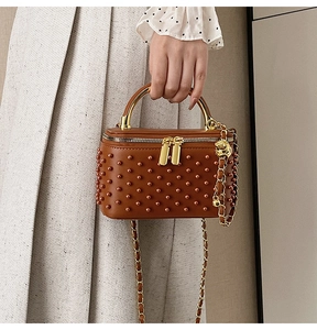 Detail of brown box bag with pearl rivets, gold chain and metallic handle