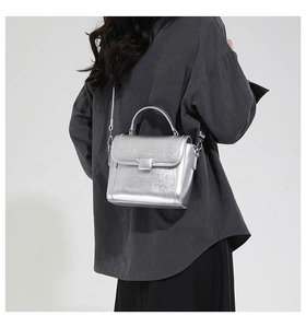 Silver metallic crossbody bag shown on model with sleek flip-top cover and metal buckle