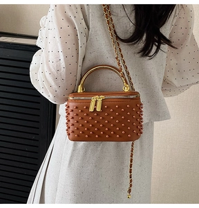 Detail view of brown rivet box bag with pearl accents and gold metal top handle