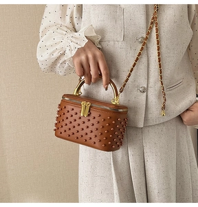 Detailed view of brown box bag with pearl studs and golden metallic handle