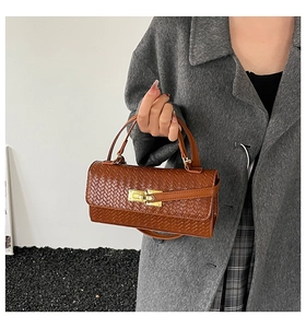 Détail d'un sac à main marron à texture tressée avec un fermoir en métal doré classique