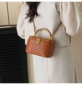 Detail of a brown vintage box bag with gold studs and a metallic top handle