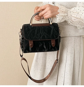 Detail of black pleated faux leather bag with golden metal handle and woven wide strap