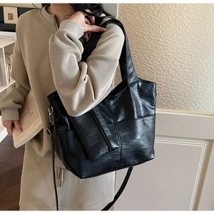 Detail of black faux leather tote bag showing fine texture and front diagonal zipper