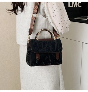 Close-up of pleated black crossbody bag with golden metal handle and jacquard strap
