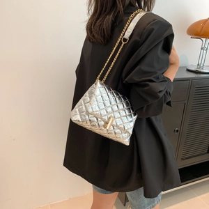 Silver quilted crossbody bag with gold chain strap on shoulder of model in black blazer