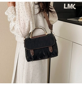 Detail of black crossbody bag featuring gold crescent metal handle and textured fabric finish