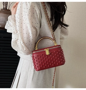 Side view of red box handbag with pearls and gold chain strap worn by a model