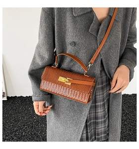 Détail du sac bandoulière marron à texture tressée et boucle dorée sur un manteau en laine