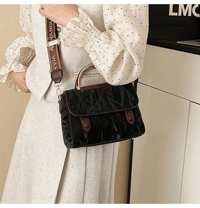 Close-up of black pleated texture shoulder bag with brown leather handle and magnetic flap