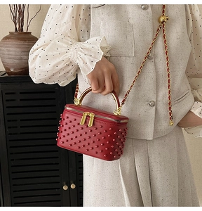 Detail of red quilted handbag with matching studs and gold circular handle worn by model