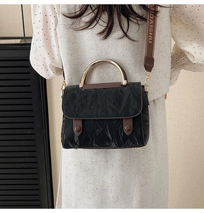 Detail of black textured handbag featuring gold metal handles and wide lettered shoulder strap