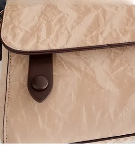 Detail shot of brown crossbody bag featuring pleated texture and round leather button closure