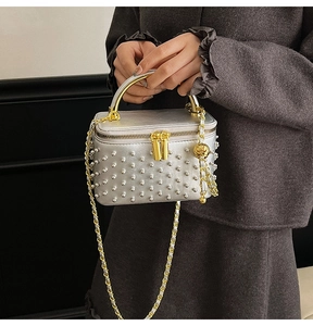 Detail of silver beaded vanity case handbag with golden handle and chain strap on grey coat