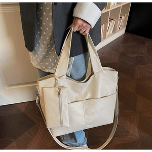 Detail of minimalist cream tote bag showing texture, side pocket and small coin purse charm