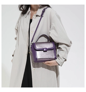 Detail of a contrasting purple and silver leather crossbody bag held by a model in a trench coat