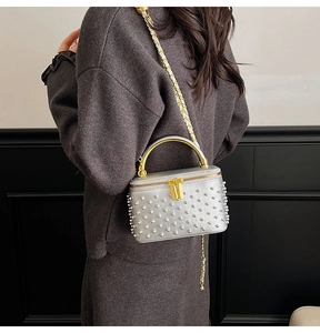 Detail of silver box bag with beaded surface, gold metal handle and chain strap