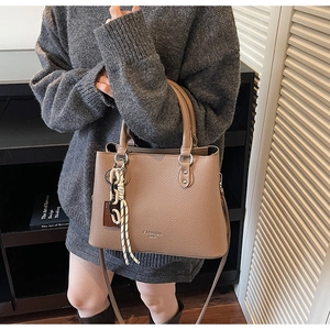 Detail of tan litchi pattern leather bag with Fashion Bag lettering and trendy pendant