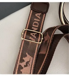 Detail of adjustable woven brown shoulder strap with golden metal buckle and woven pattern