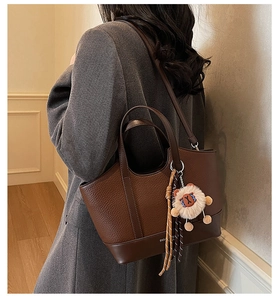 Detailansicht der braunen Leder-Eimertasche mit Löwen-Plüschtier und Schultergurt