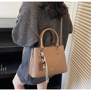 Detail view of deep camel litchi grain leather bag with decorative charms and metal feet