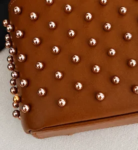 Macro detail of brown leather bag featuring studded bead texture and premium stitching