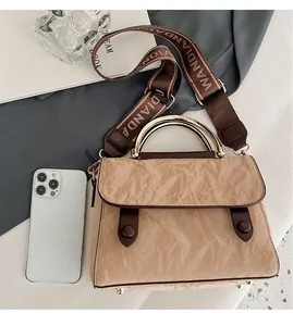 Detail of pleated beige handbag with brown leather trim and golden metal handle