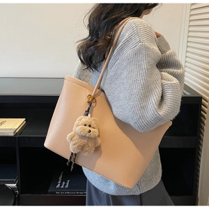 Beige tote bag van korrelig leer met beertje hanger gedragen door een model in trui