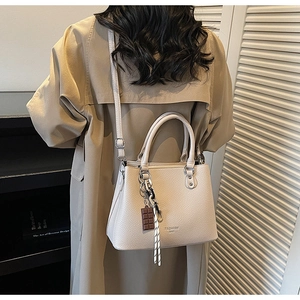 Detail view of off-white lychee pattern leather handbag with creative chocolate charm strap