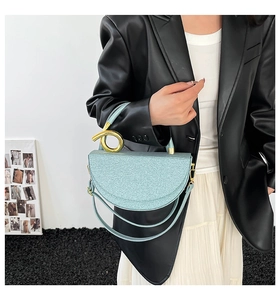 Detail of light blue glitter saddle bag with sculptural gold handle and metallic texture