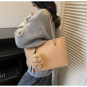 Detail van beige tas met korrelstructuur, beertje hanger en lint op grijze trui