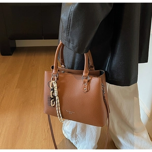 Brown lychee leather tote bag with braided charm shown in a cozy home setting