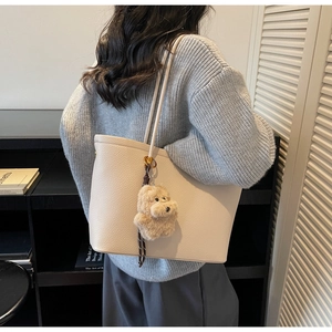 Detail van beige tas met litchi-patroon en schattige hondenknuffel aan de schouder