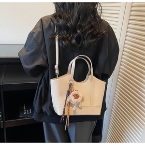 Detailansicht der beigen Eimer-Tasche mit Litschistruktur, Logo und Plüsch-Anhänger