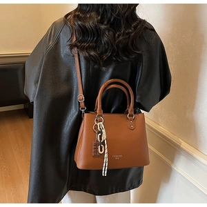 Detail of brown litchi pattern leather handbag with fashion charms and crossbody strap