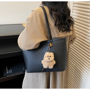 Detail van zwarte tas van generfd leer met een beige pluche hondenhanger aan de riem