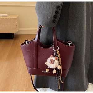 Detail der burgunderroten Bucket Bag aus genarbtem Leder mit Logo und Taschenanhänger