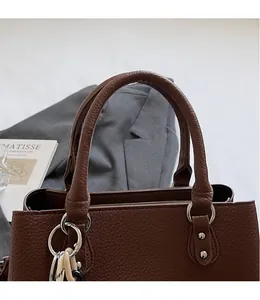 Close-up of litchi grain leather texture and durable handles on brown handbag