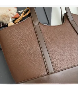 Detailaufnahme der braunen Litschi-Lederstruktur und Plüsch-Anhänger an einer Beuteltasche