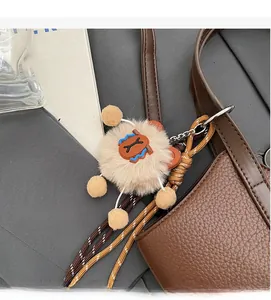 Detail eines Plüschbär-Anhängers mit gewebtem Riemen an einer Lederhandtasche