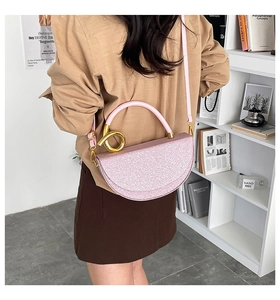 Detail of pink glitter saddle bag with golden ring handle on a female shoulder