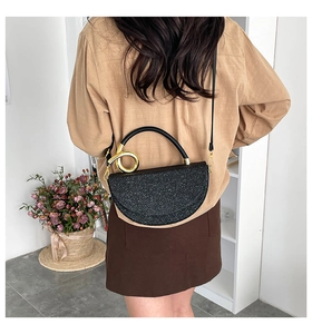 Detailed view of a black glitter crescent bag with gold hardware worn by a model