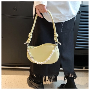 Detail of light yellow half-moon bag featuring pearl chain and silver heart charm